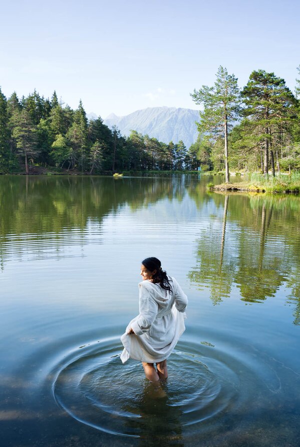 Woman in white dress standing in lake, trees and mountains in background