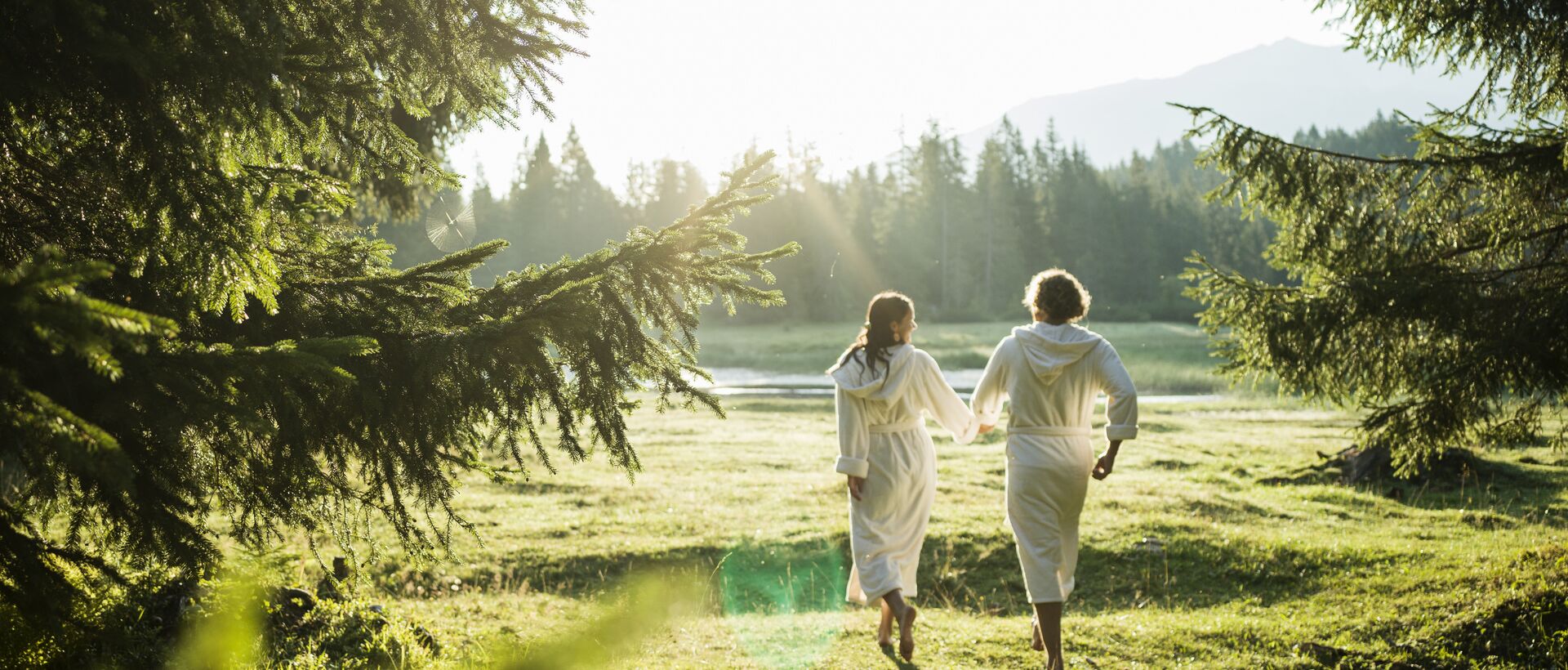 Two people in bathrobes walking hand in hand across a meadow