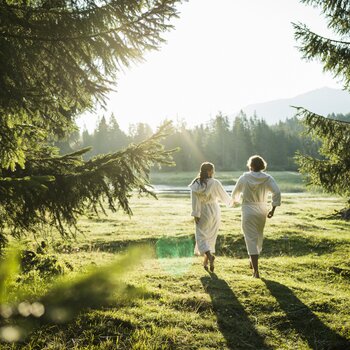 Two people in bathrobes walking hand in hand across a meadow