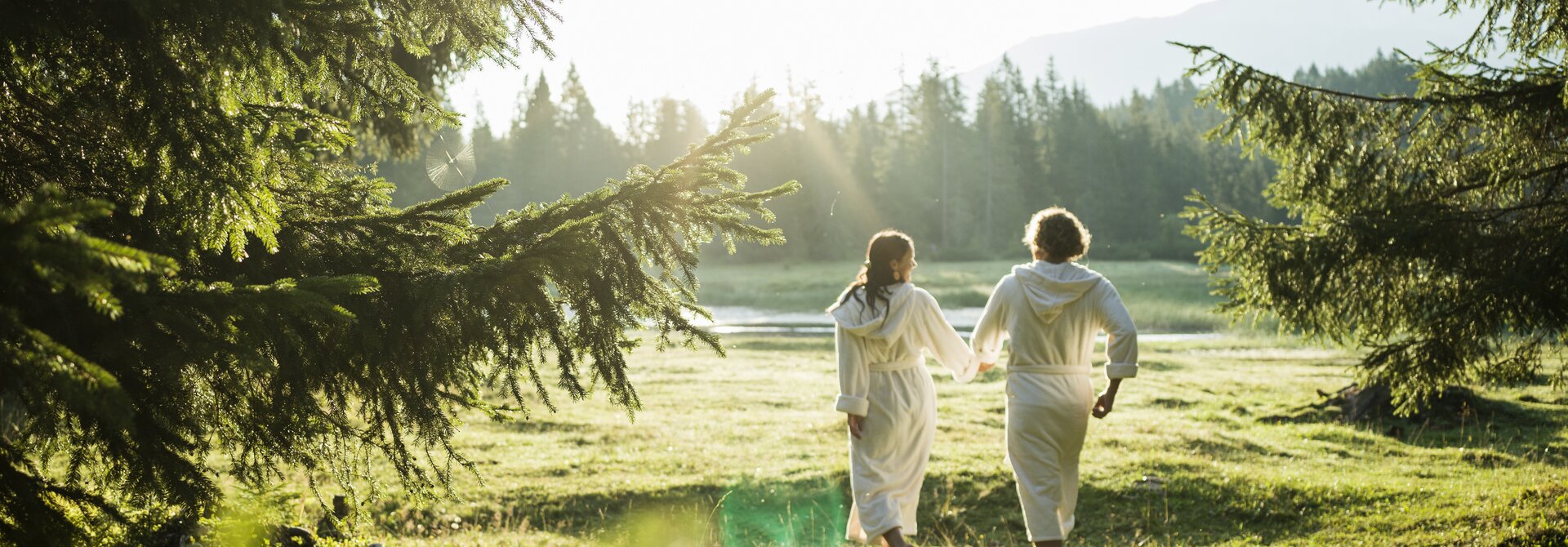 Two people in bathrobes walking hand in hand across a meadow
