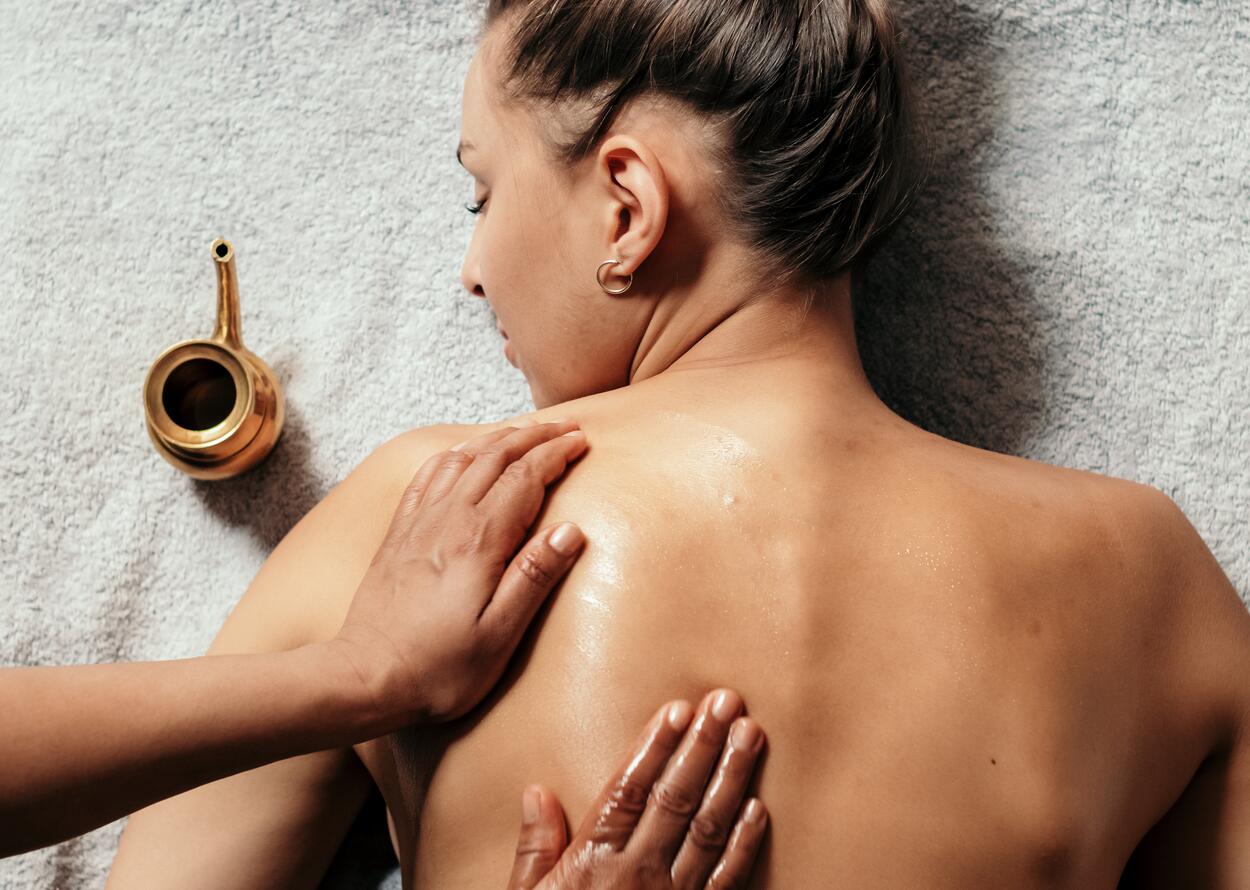 Woman lying on her stomach, being massaged with oil, golden jug next to her
