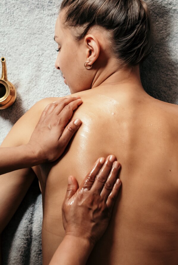 Woman lying on her stomach, being massaged with oil, golden jug next to her