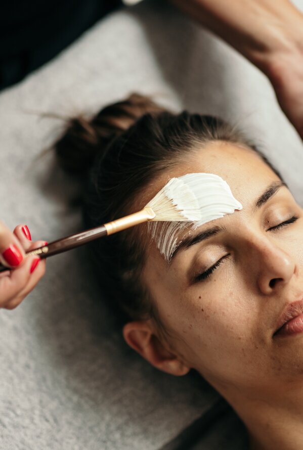 Woman receiving facial treatment with brush and white cream