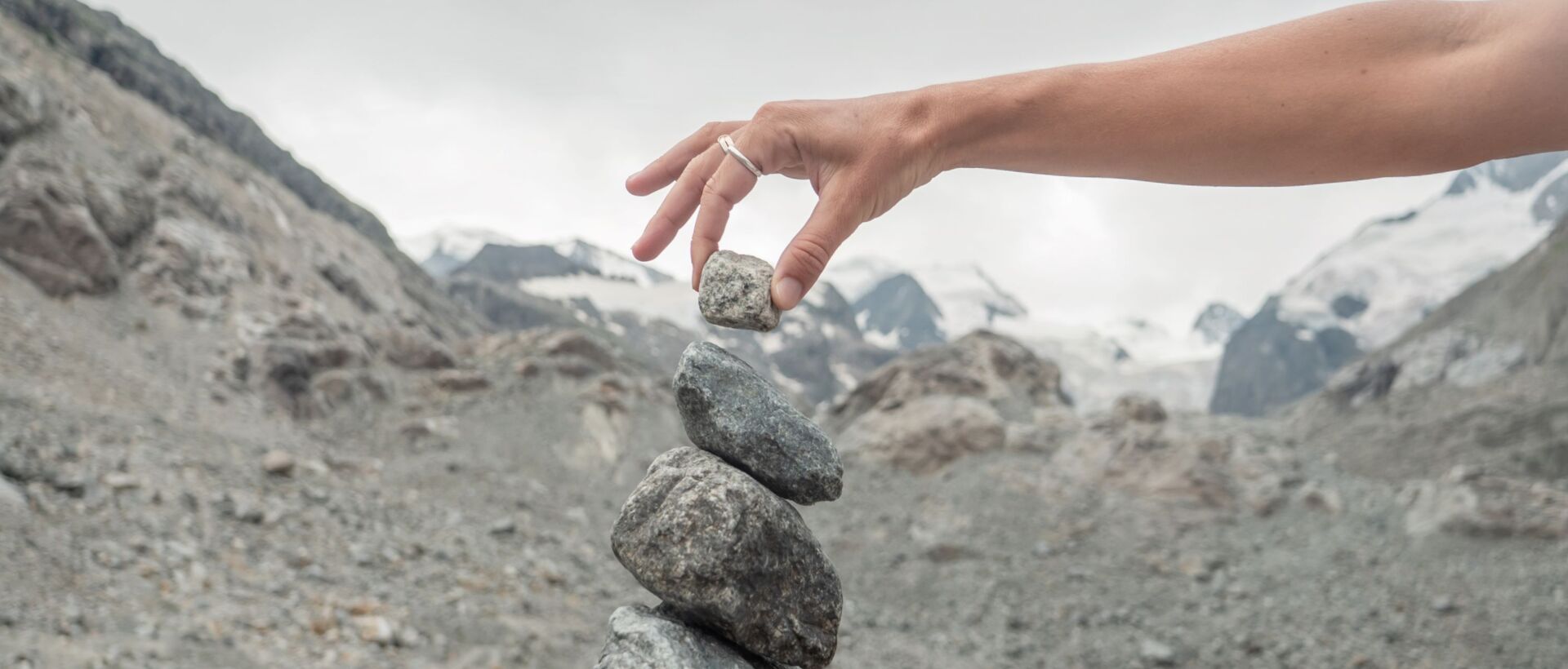 Hand hält Stein vor grauer Berglandschaft und bewölktem Himmel