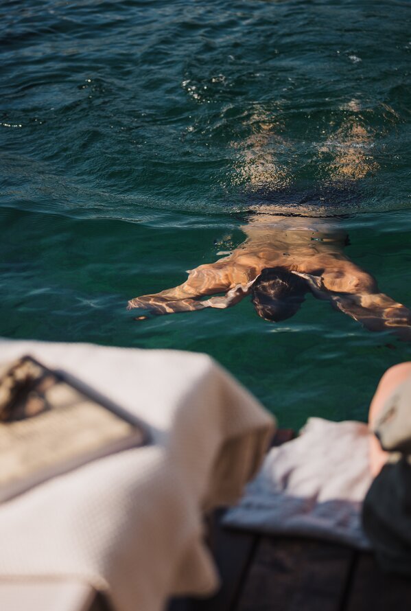 Person schwimmt im Wasser, während jemand am Ufer sitzt.