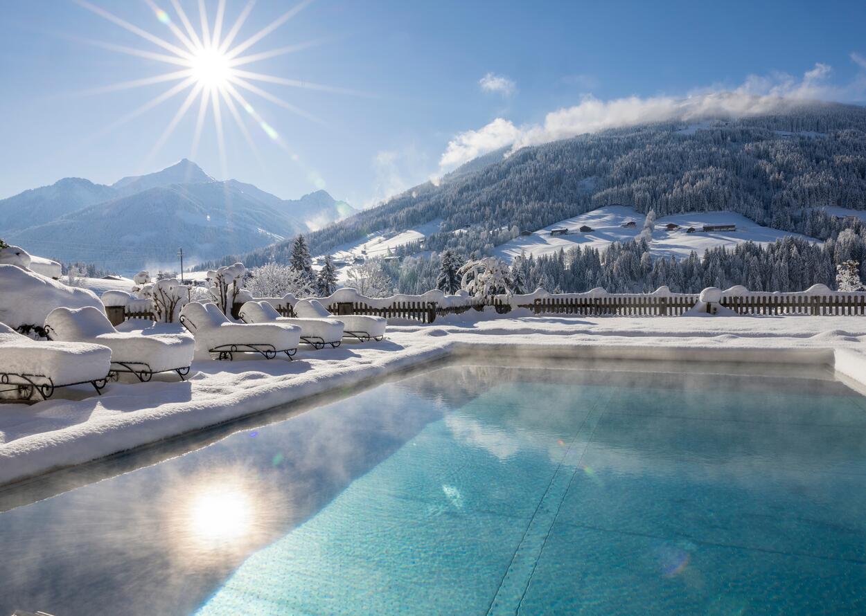 Winterlicher Pool vor verschneiter Berglandschaft im Sonnenschein