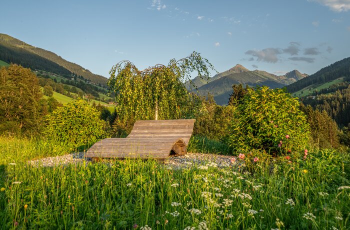 Holzliege im Grünen vor Bergpanorama bei Abendstimmung