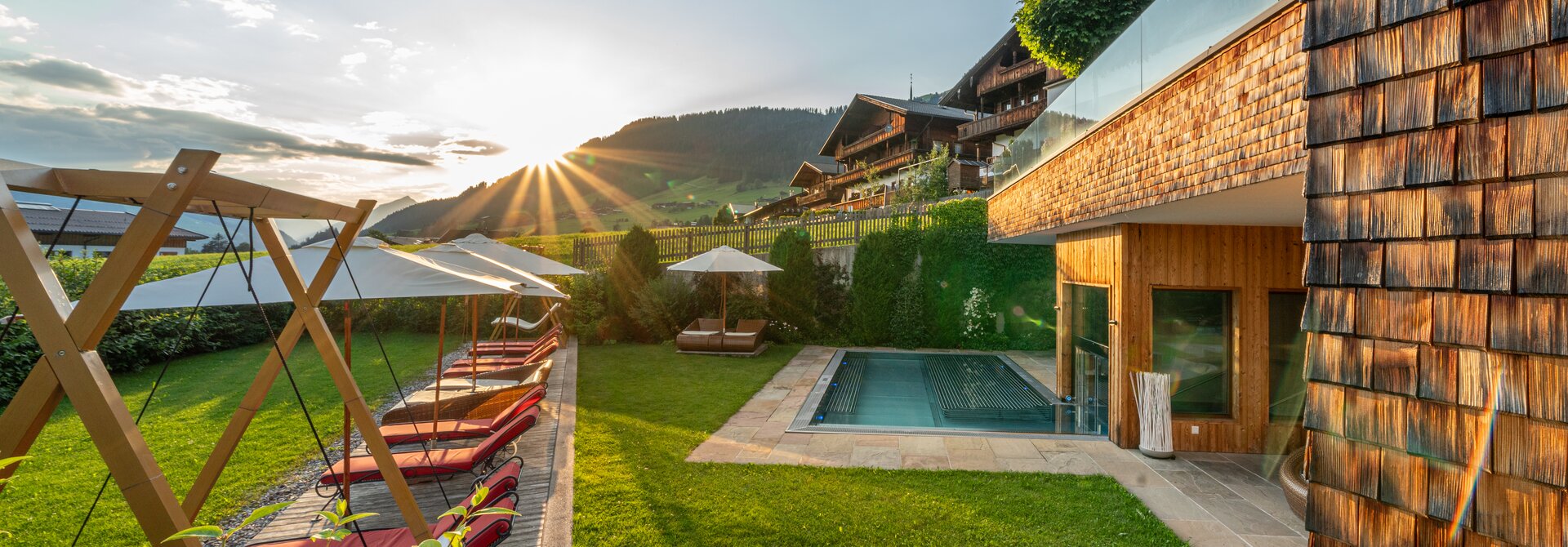 Außenbereich mit Pool, Sonnenliegen und Bergblick bei Sonnenuntergang
