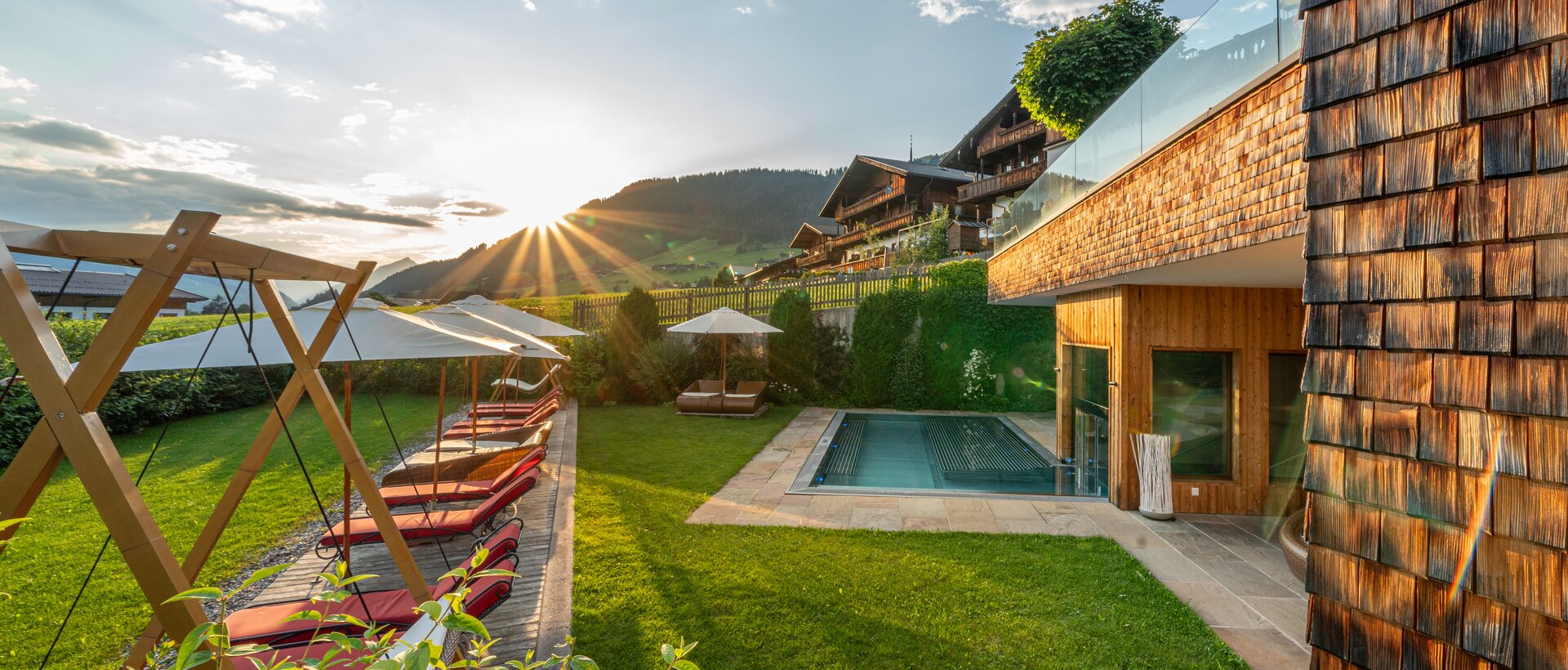 Außenbereich mit Pool, Sonnenliegen und Bergblick bei Sonnenuntergang