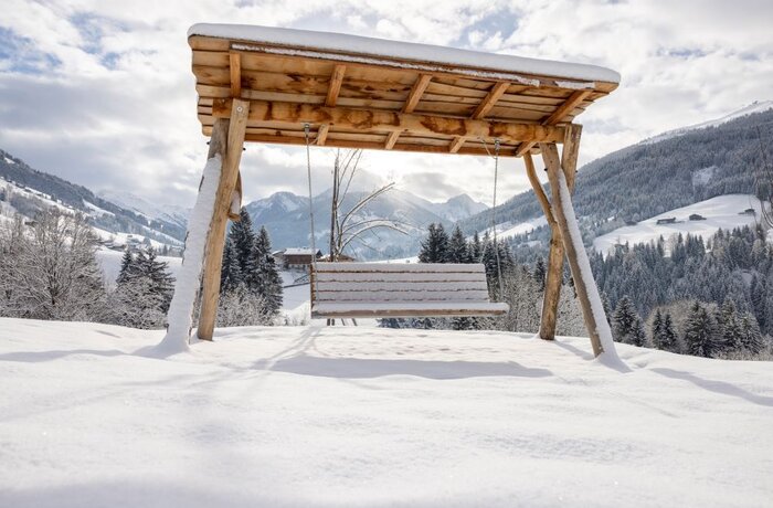 Schaukel mit Dach im verschneiten Garten vor Berglandschaft
