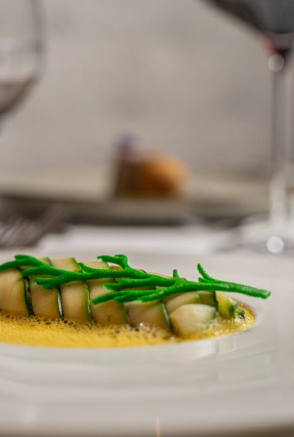 Fischgericht mit grünen Kräutern auf Teller, zwei Weingläser im Hintergrund