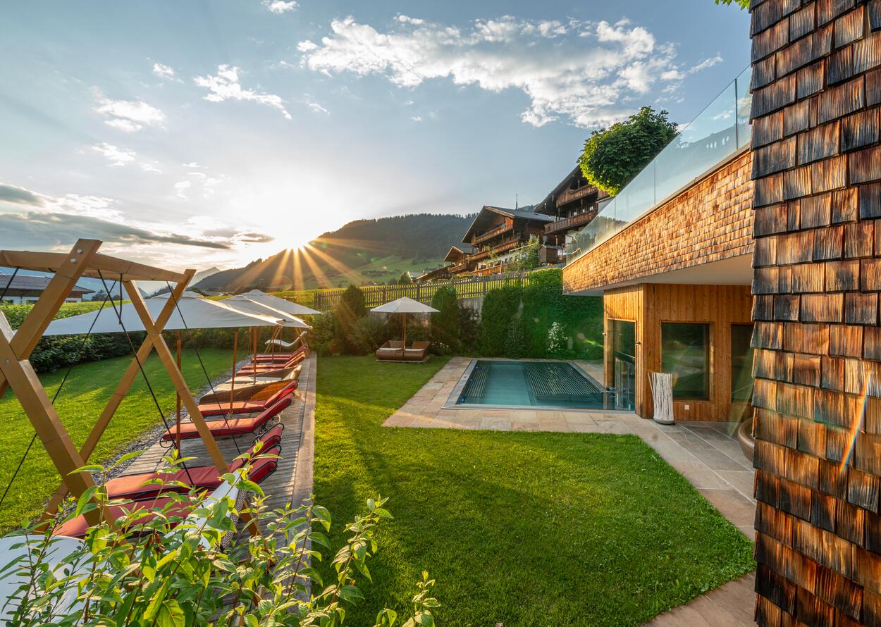 Außenbereich mit Pool, Sonnenliegen und Bergblick bei Sonnenuntergang