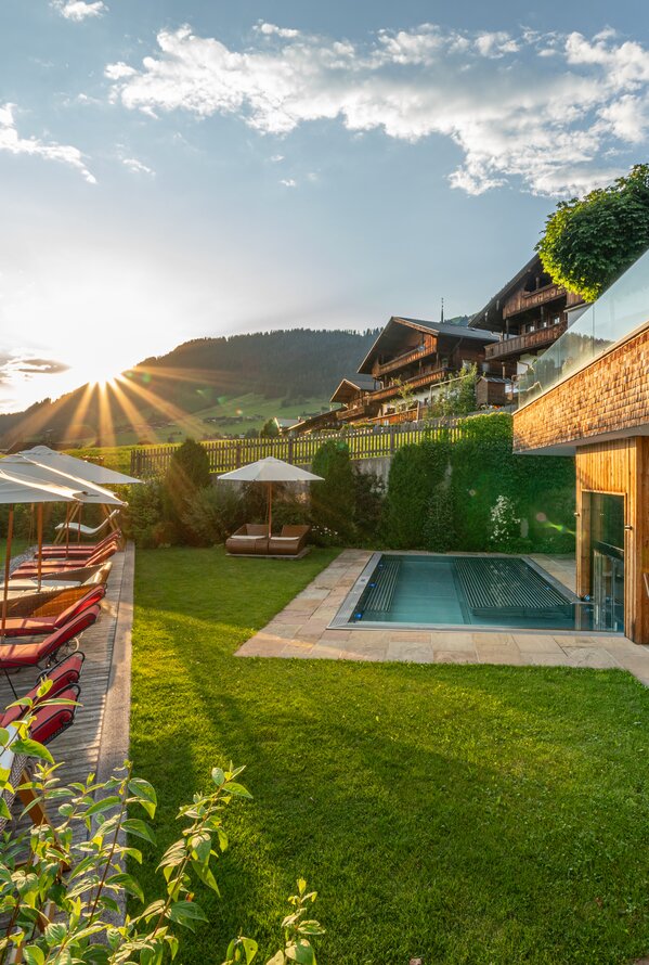 Außenbereich mit Pool, Sonnenliegen und Bergblick bei Sonnenuntergang