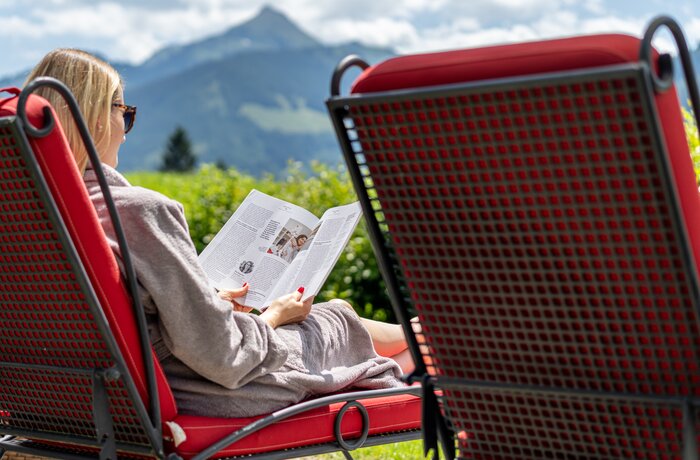 Frau liest in roter Liege vor Bergkulisse