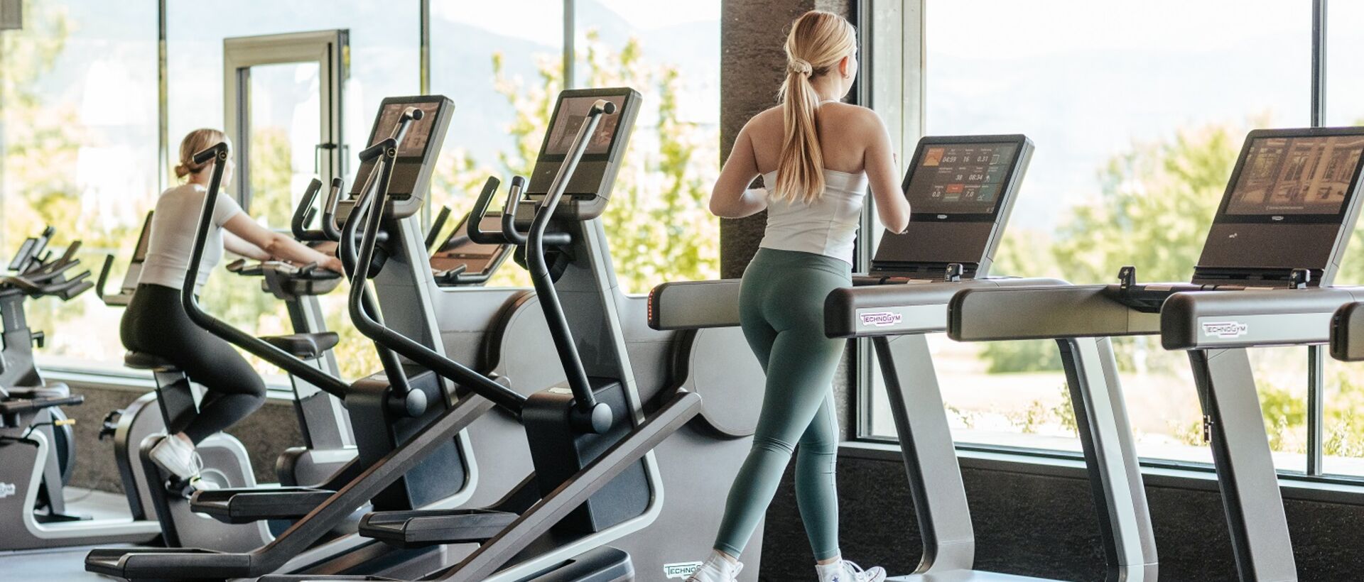 Frau läuft auf Laufband in hellem Fitnessstudio mit Blick ins Grüne