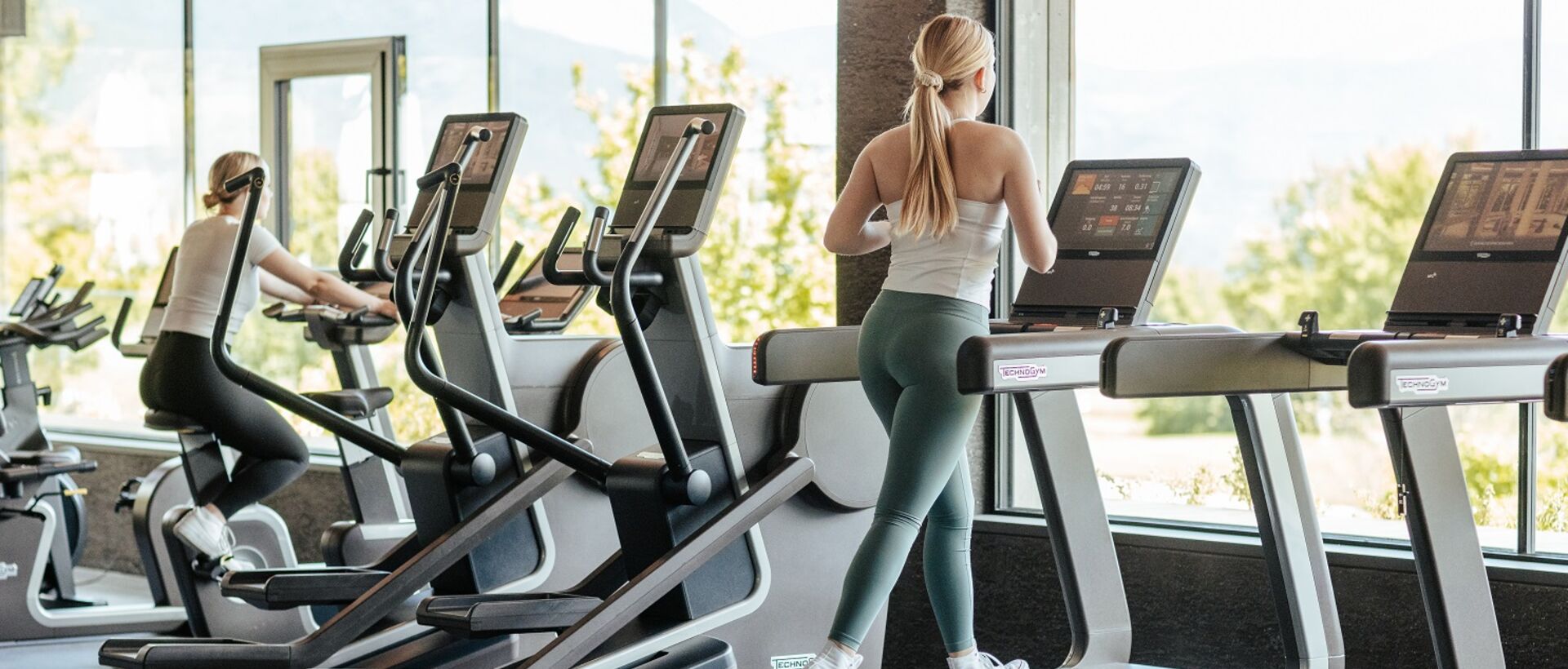 Woman running on treadmill in bright gym with view of greenery