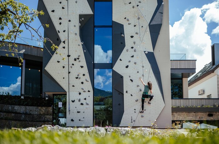 Woman climbing on a grey climbing wall with a window front on a building