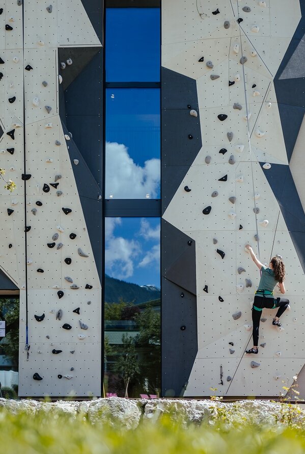 Woman climbing on a grey climbing wall with a window front on a building