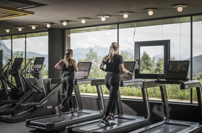 Two women train on treadmills in a gym with panoramic windows