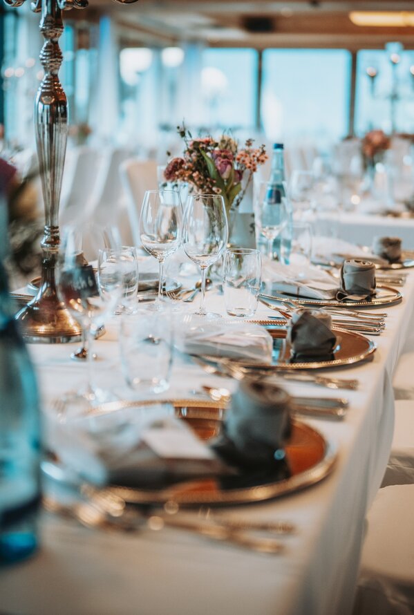 Festlich gedeckte, lange Tafel mit Blumen und Getränken in hellem Raum