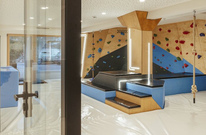 Moderner Indoor-Spielraum mit Kletterwand, Seilen und weichen Spielflächen für Kinder.