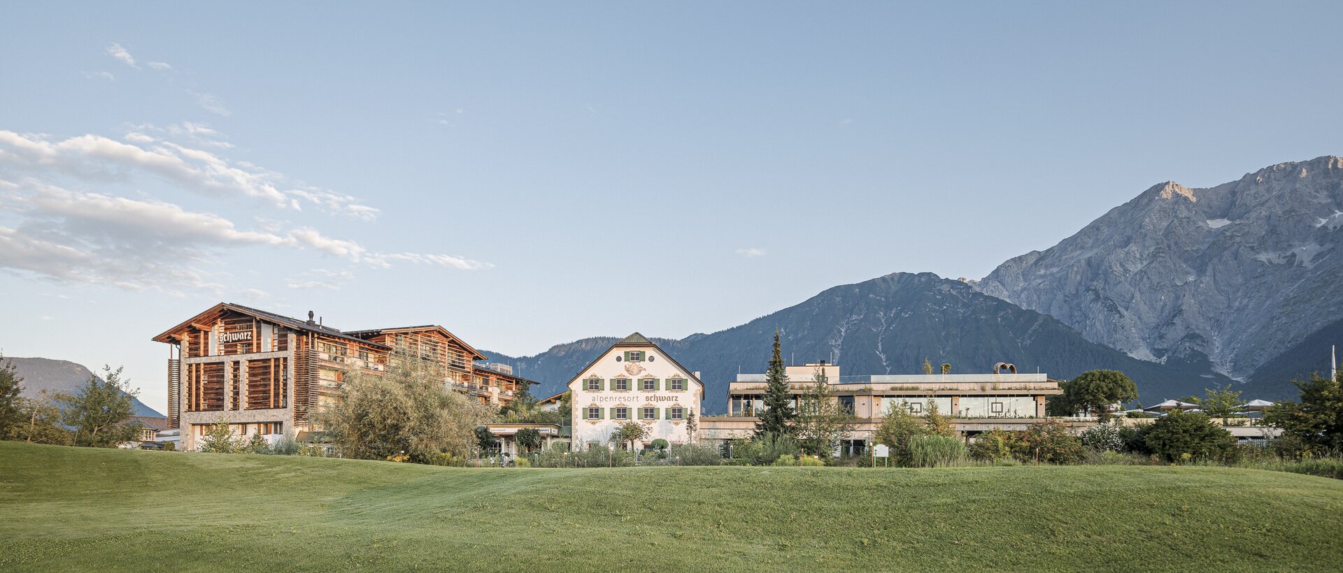 Alpenresort Schwarz in front of green meadow and mountain backdrop under blue sky