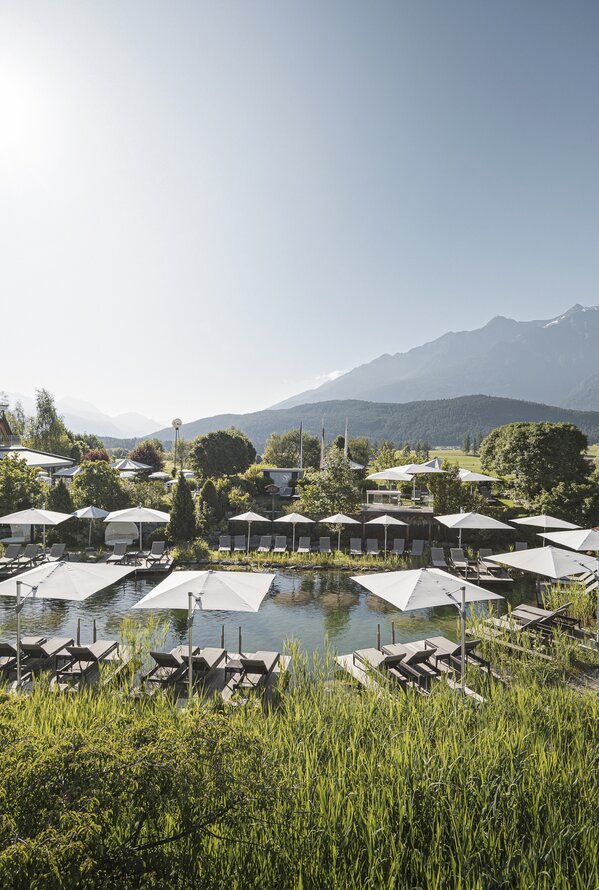 Naturpool im Alpenresort Schwarz mit Liegebereich und Blick auf die Tiroler Berglandschaft