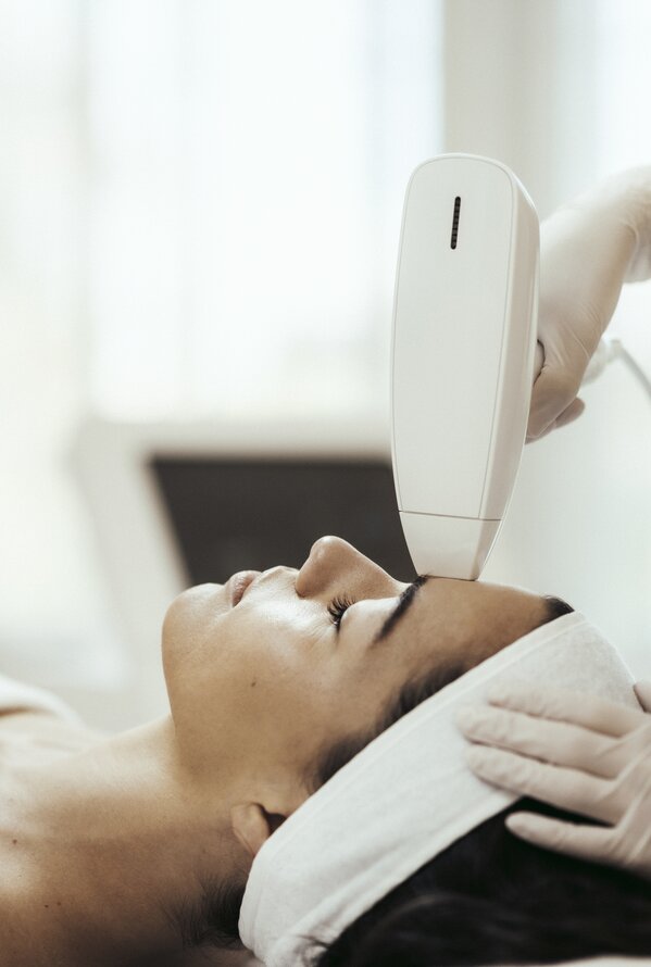 Woman lying down during facial treatment with white device and gloves