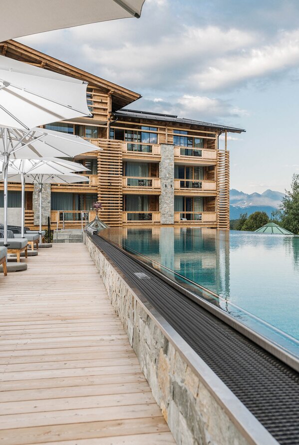 Außenbereich eines Wellnesshotels mit Pool, Liegen und Sonnenschirmen vor einer Holzfassade