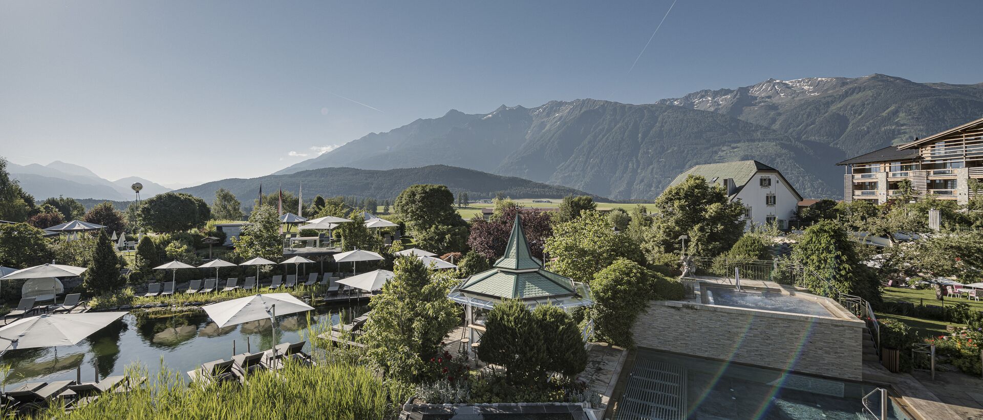 Alpenresort Schwarz mit Pool, Pavillon und Liegen vor Bergpanorama an einem sonnigen Tag