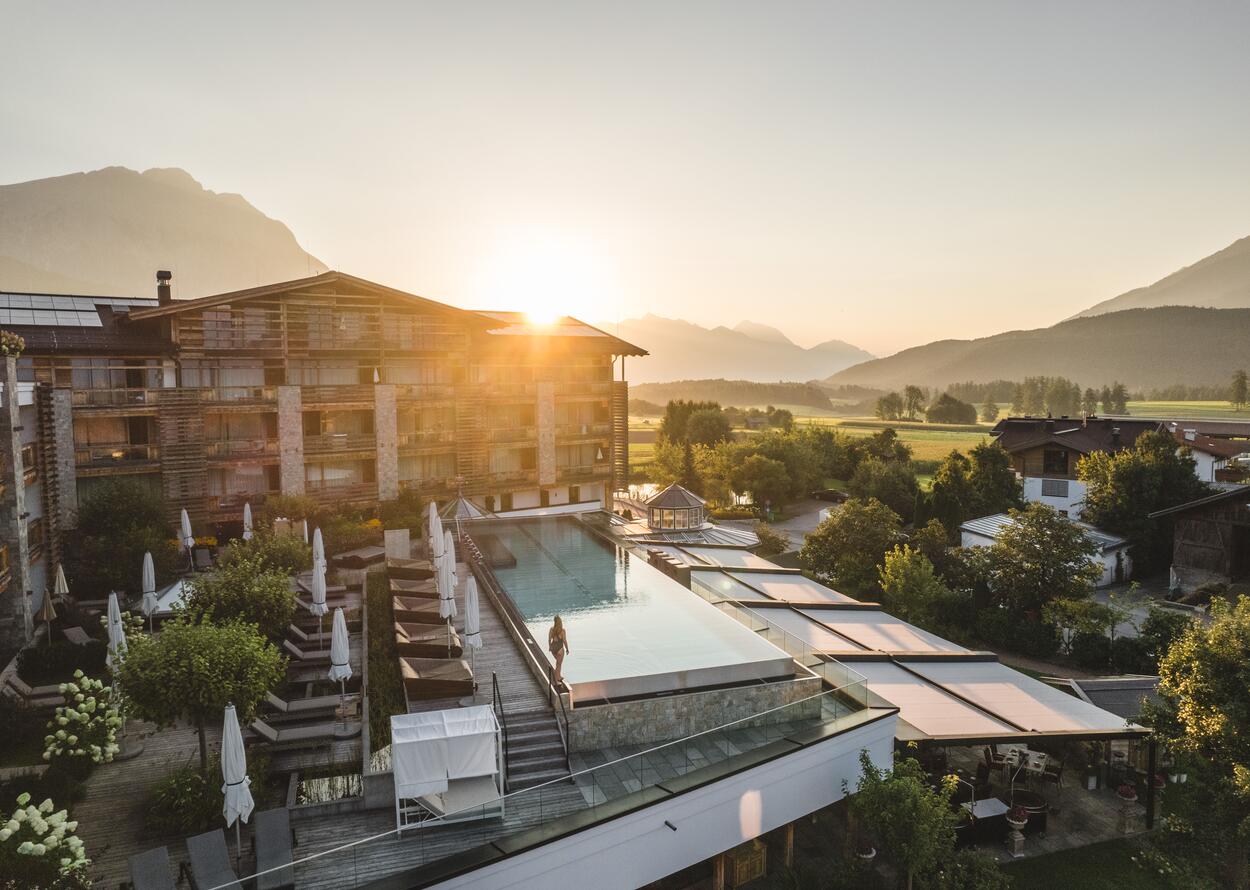 Luftaufnahme eines Hotels mit Infinity-Pool und Bergpanorama bei Sonnenuntergang