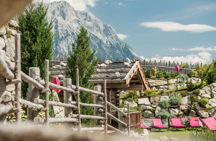 Poolbereich mit Holzhütte, Liegen und Bergpanorama im Hintergrund