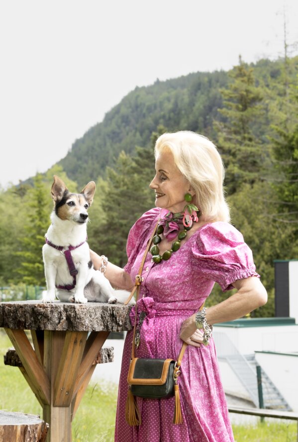 Elisabeth Gürtler mit Hund auf Baumstumpf vor Bergkulisse