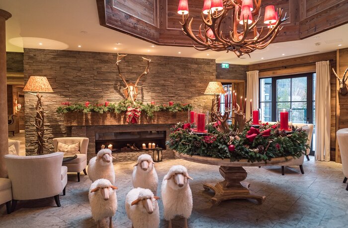 Adventskranz mit roten Kerzen und Deko-Schafen in Hotel-Lobby mit Kamin und Geweih-Leuchter