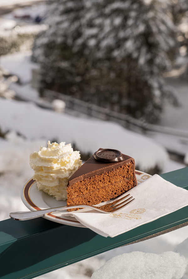 Sacher-Torte mit Sahne auf Teller vor verschneiter Winterlandschaft