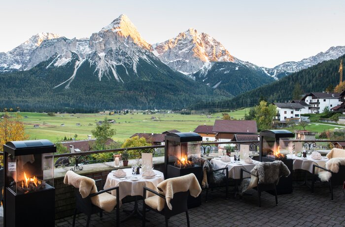 Hotelterrasse des Hotel Post mit Tischen, Stühlen und Kaminfeuer vor Bergpanorama im Herbst