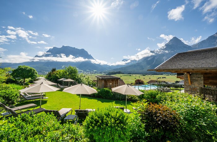 Grüne Wiese mit Liegen und Sonnenschirmen vor Bergpanorama unter strahlender Sonne