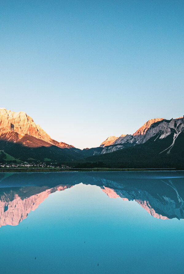 Ruhiger Bergsee mit beeindruckender Spiegelung der Berge im Abendlicht.