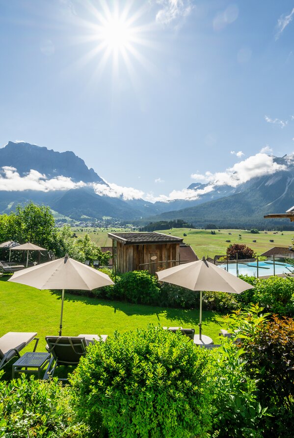 Sonniger Wellnessgarten mit Liegen, Sonnenschirmen und weitem Blick auf die Berge.