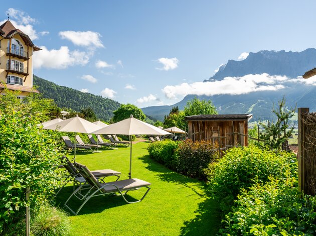 Ruhiger Gartenbereich mit Liegen und Sonnenschirmen vor beeindruckender Bergkulisse.