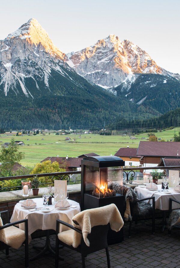 Hotelterrasse des Hotel Post mit Tischen, Stühlen und Kaminfeuer vor Bergpanorama im Herbst