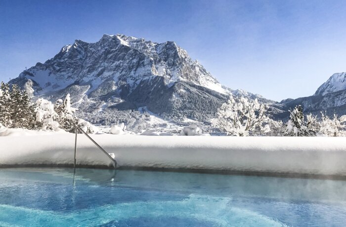 Winterlicher Pool mit Blick auf die schneebedeckte Zugspitze unter blauem Himmel