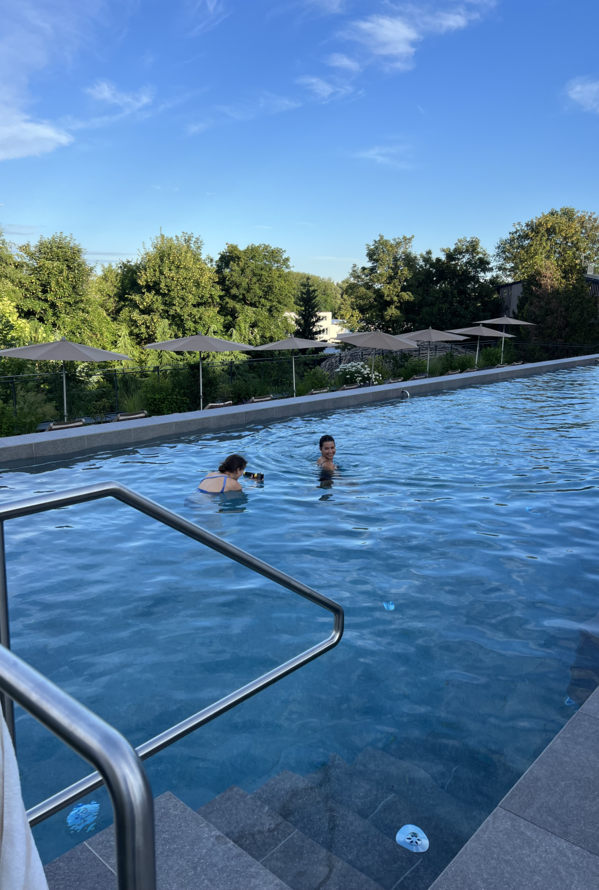 Zwei Personen schwimmen in einem langen Außenpool mit Sonnenschirmen am Rand