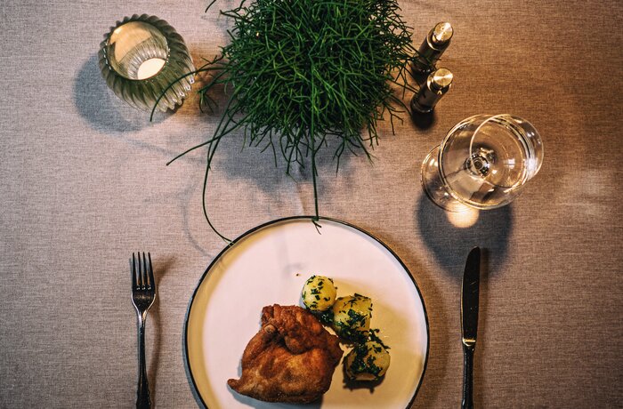 Gedeckter Tisch mit Teller, Fleisch, Kartoffeln, Besteck, Glas, Kerze und grüner Dekoration