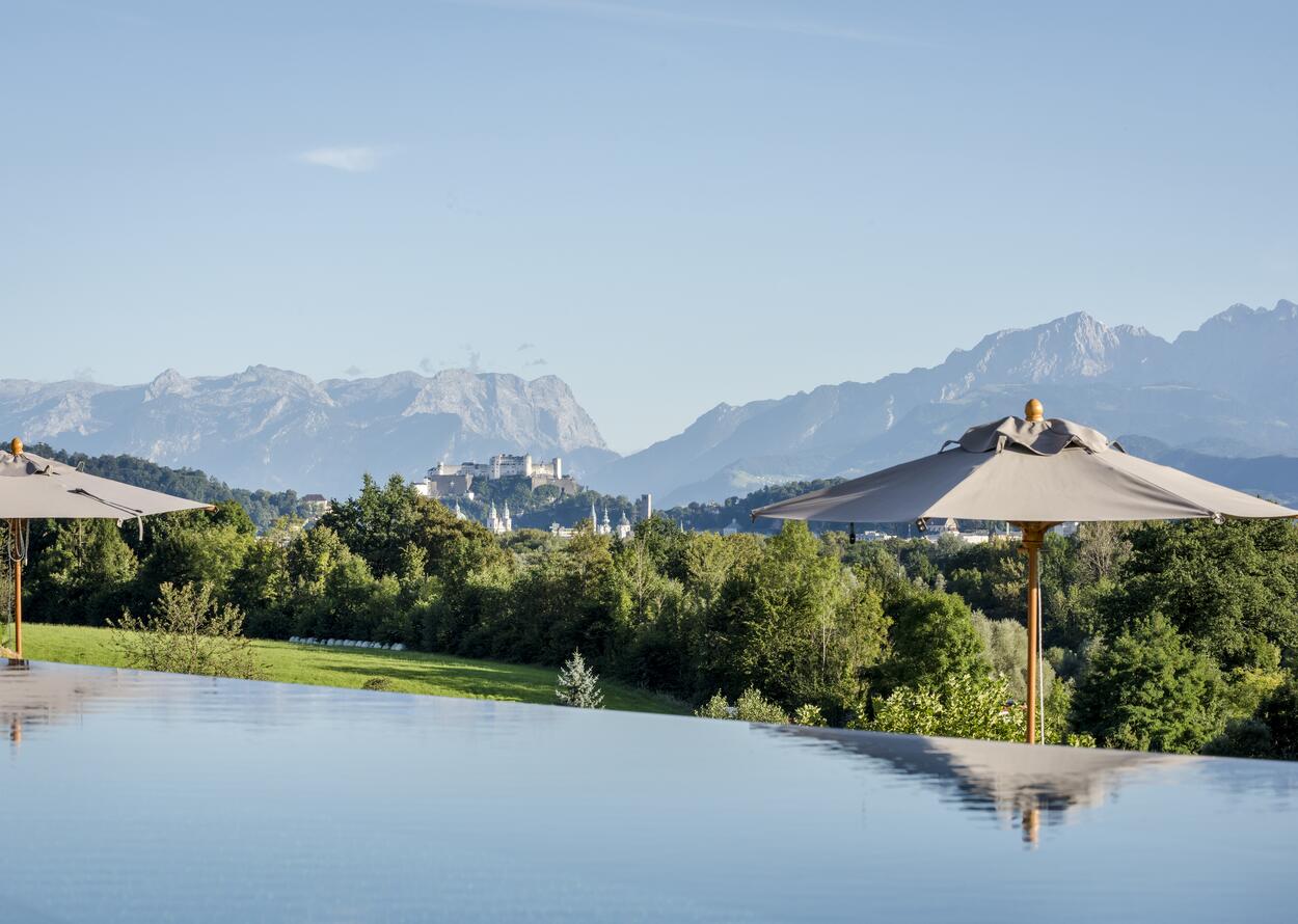 Infinity-Pool mit beeindruckendem Alpenpanorama und Blick auf die Festung Salzburg inmitten grüner Natur.