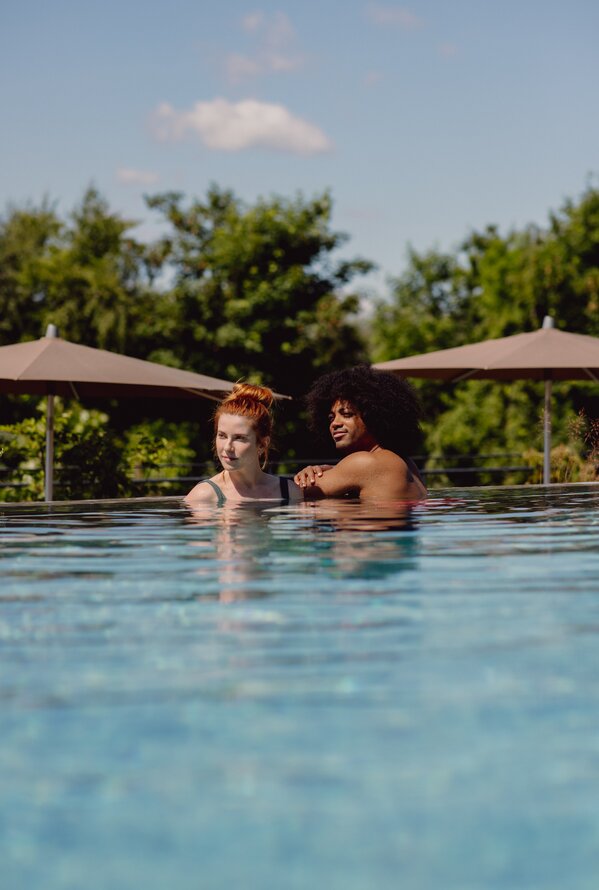 Zwei Personen im Pool, Bäume und Sonnenschirme im Hintergrund