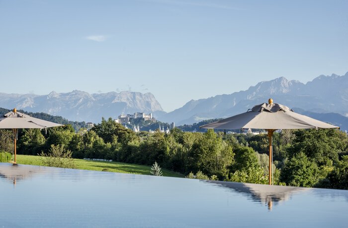Infinity-Pool mit beeindruckendem Alpenpanorama und Blick auf die Festung Salzburg inmitten grüner Natur.