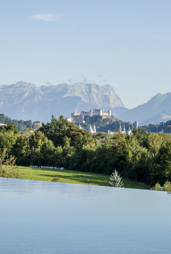 Infinity-Pool mit beeindruckendem Alpenpanorama und Blick auf die Festung Salzburg inmitten grüner Natur.