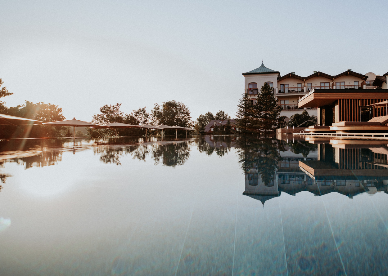 A calm pool reflects a hotel and the evening sky.
