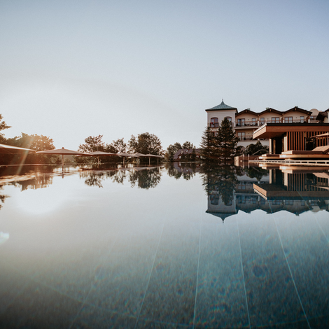 A calm pool reflects a hotel and the evening sky.